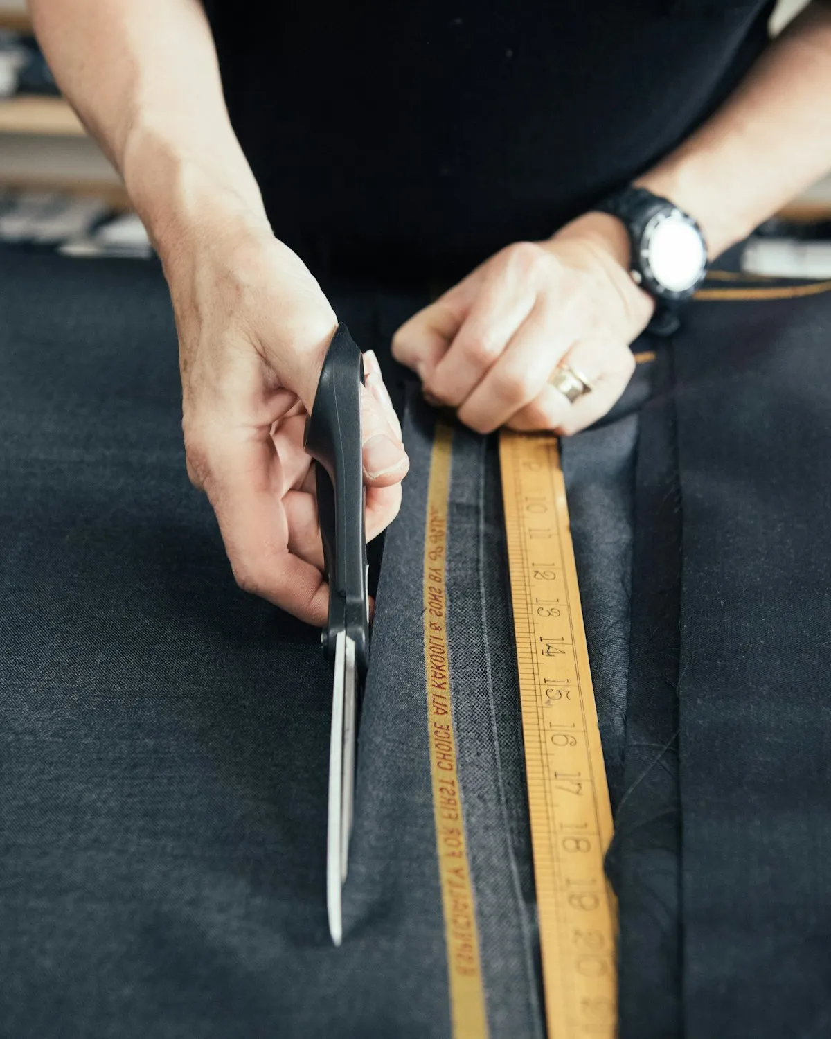 Hands cutting a length of cloth with shears at the worktable.