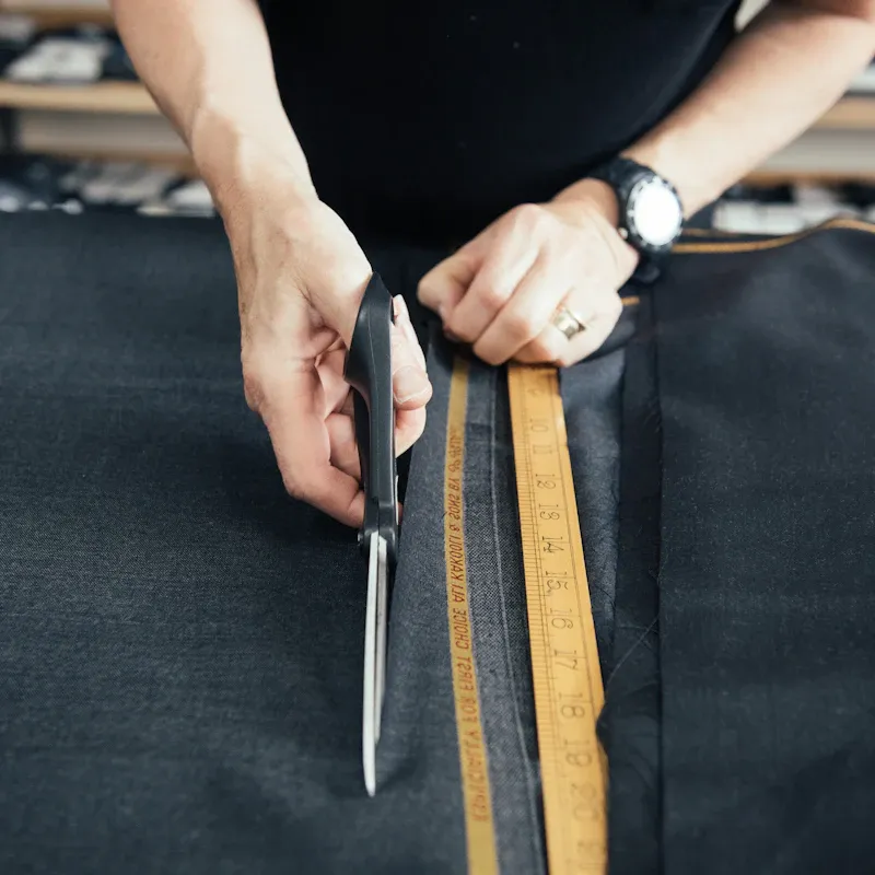 Hands cutting a length of cloth with shears at the worktable.