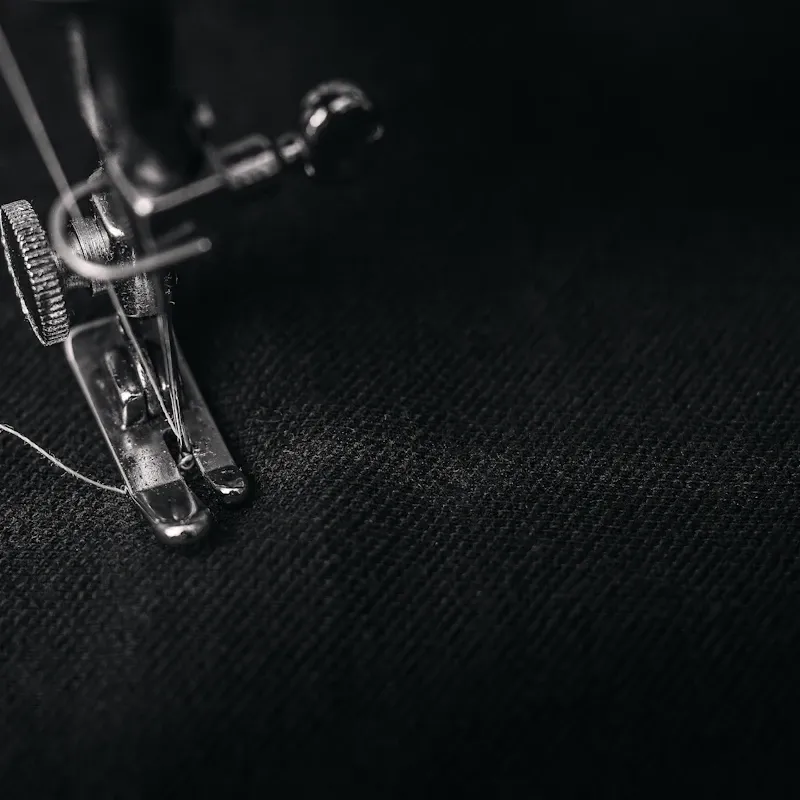 A needle and presser foot working a seam on dark cloth.